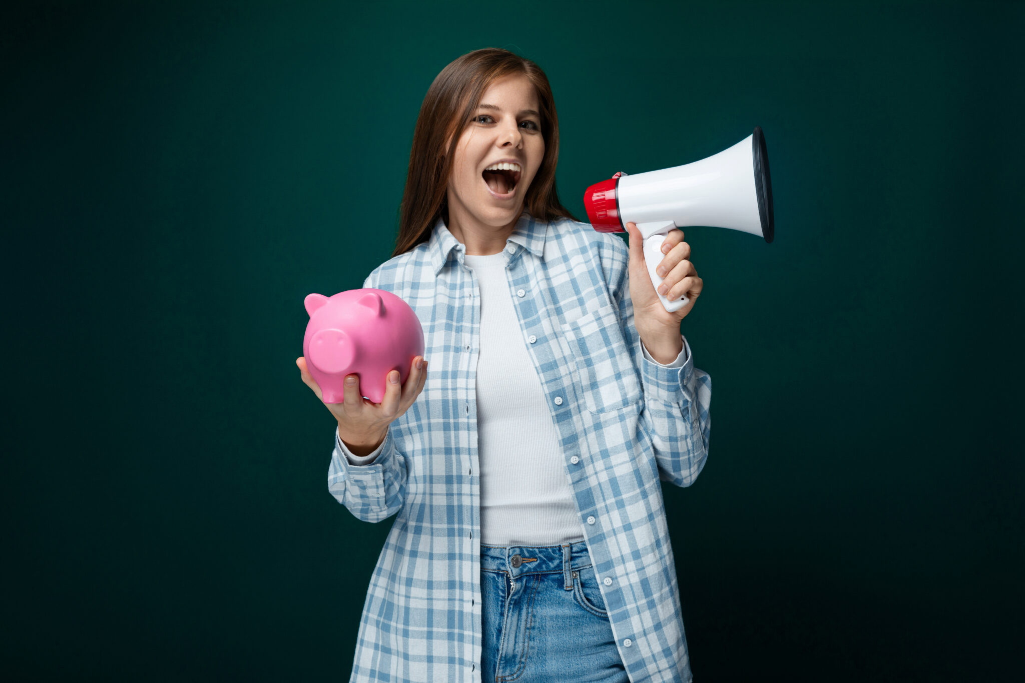 Young European woman dressed in a plaid shirt and jeans holds a piggy